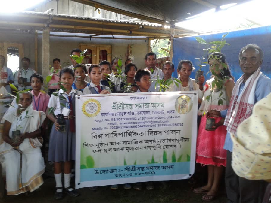 Schoolchildren holding saplings beside the SRI SRI SANTA SAMAJ World Environment Day banner